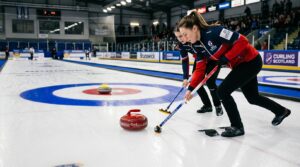 Curlingstenar glider mot boet på isen under sopning av curlingspelare