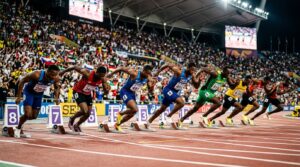 Sprinters i startblocken på en löparbana inför 100 meter med arena och strålkastare i bakgrunden